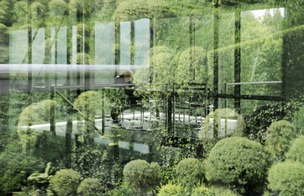 Fig. 1: Foto of the Experimental House R128 glass façade with combination of visual reflection (exterior greenery) and visual transmittance (interior furniture and person).