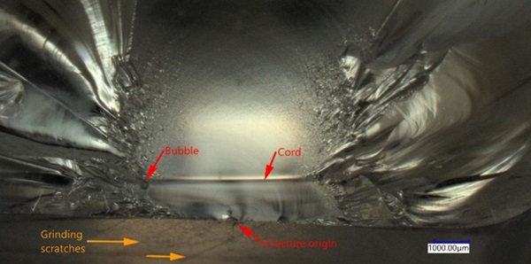 Fig. 37: Simultaneous action of different defects around the fracture origin of a recycled cast borosilicate specimen, tested in bending. Cord and bubbles in the bulk interact with the crack front path, yet, it is the grinding scratches at the surfacethat cause the fracture of the component.