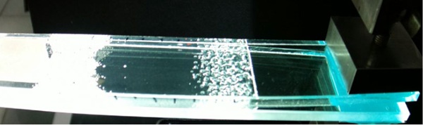 Fig. 6: At room temperature and at a speed of 1m/min, the standard PVB interlayer delaminates in relatively slow propagation of the delamination front. A steady state regime in which the delamination is occurring with a large deformation of the interlayer and cavitation ahead of the delamination front.