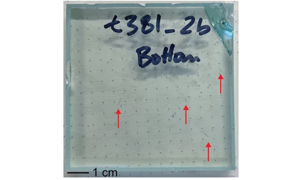 Fig. 8: Photograph of preliminary test sample (7.5 x 7.5 cm) which failed during compression testing. Failure occurred when the test sample was loaded far beyond the initial buckling step. Red arrows indicate areas where local scratches were made from kirigami. Edge chips can also be seen. Top right fracture is the location of fracture during testing.