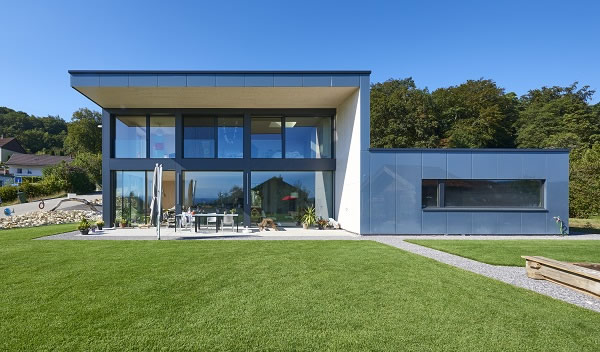 On the south-facing aspect, the structure opens up to the outside with a large glass façade. Subtle reflections mirror the surroundings.