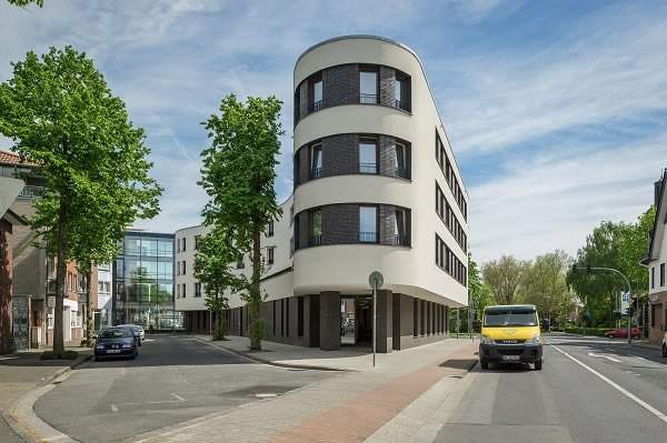The three upper floors of the boomerang-shaped building structure protrude into the public space. The ribbon windows provide a contrast to the light façade and emphasise the horizontal extension of the building.