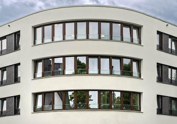 The three upper floors of the boomerang-shaped building structure protrude into the public space. The ribbon windows provide a contrast to the light façade and emphasise the horizontal extension of the building.