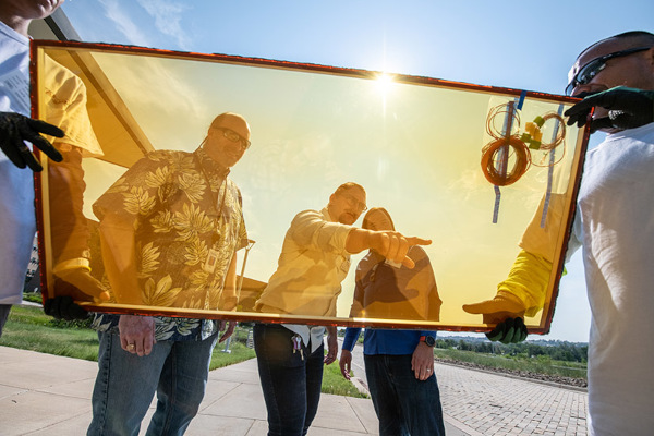 Rob Tenent, lead researcher for NREL’s windows projects (left), watches the installation of UbiQD’s windows at the laboratory’s Café. The company’s laminated glass absorbs sunlight, which then generates electricity. Photo by Dennis Schroeder, NREL