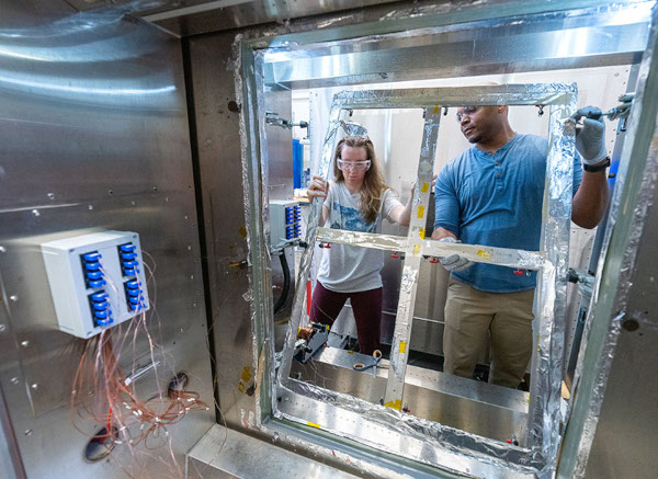 Madison Likins-White, a fellow in the DOE Office of Energy Efficiency and Renewable Energy’s Building Technologies Office Innovations in Building program, and NREL researcher Alliston Watts install an insulating glass unit into a Differential Thermal Cycling Unit. The device measures thermal performance as part of ongoing research into field evaluation of insulating glass performance to develop models of how performance degrades in the field over time. Photo by Werner Slocum, NREL