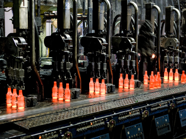 Red-hot glass bottles right after being moulded: in the IS machine the molten glass receives its final shape before the containers are fed to the annealing lehr. Photo: Bundesverband Glasindustrie e.V. (BV Glas)
